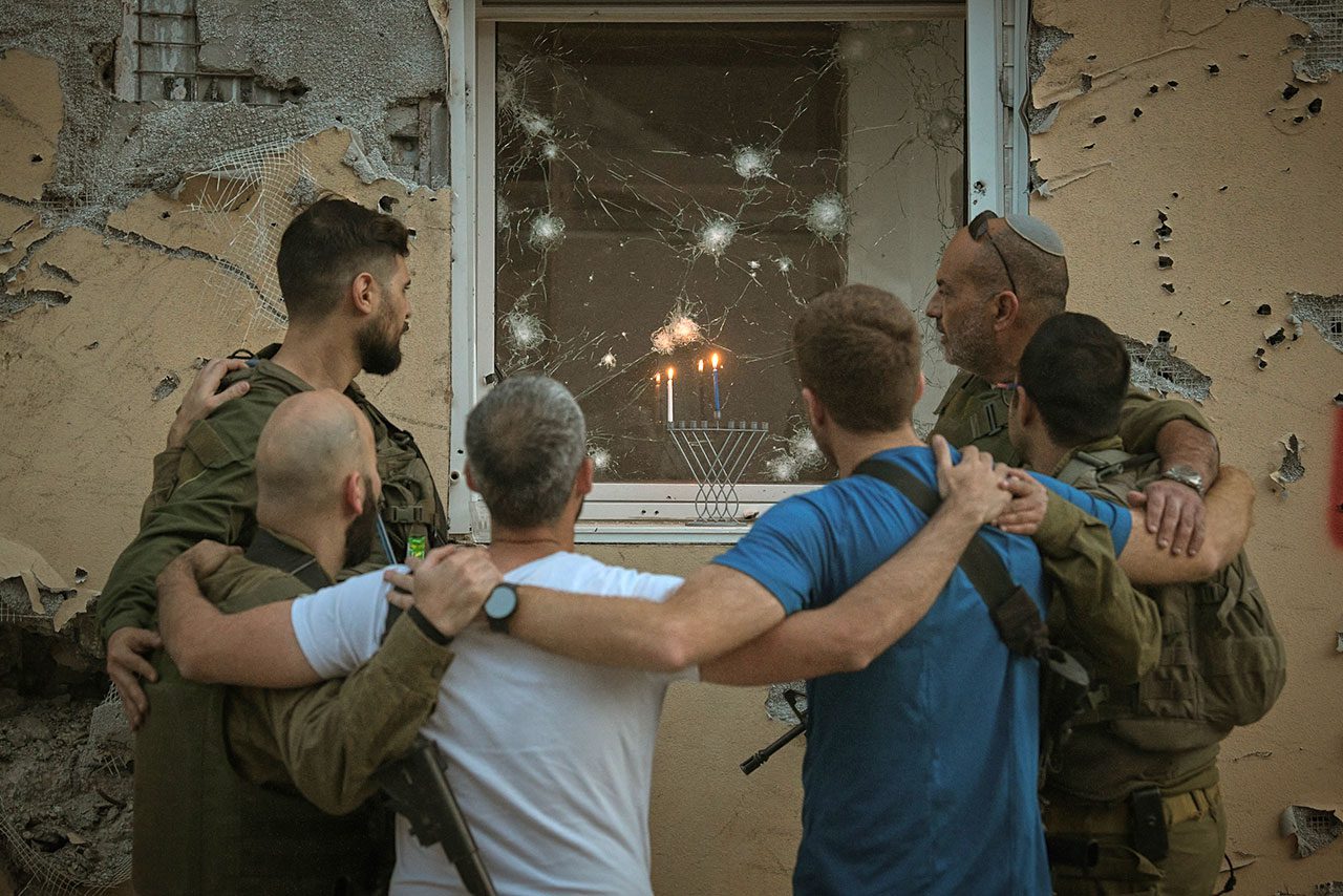 חיילים מדליקים נר ראשון של חנוכה על אדן חלון הממ״ד של בית הרוס, קיבוץ בארי