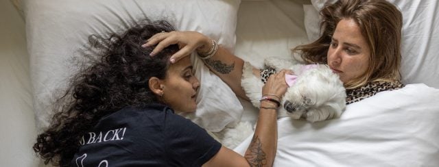 HOLD FOR STORY. Emily Damari wakes up on the morning of her 29th birthday alongside her partner, Danielle Amit, (right) and Mayo, Danielle’s dog. Rishpon, Israel, June 10, 2025. Avishag Shaar-Yashuv for The New York Times. Danielle Amit is Emily’s first partner since her return from captivity. She is a well-known food influencerl, and the publication of their relationship caused a stir in Israel.